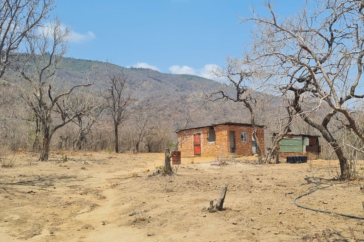 A rustic, small brick structure situated on a dry, rural farm landscape with mountain views, requiring significant renovation or redevelopment.
