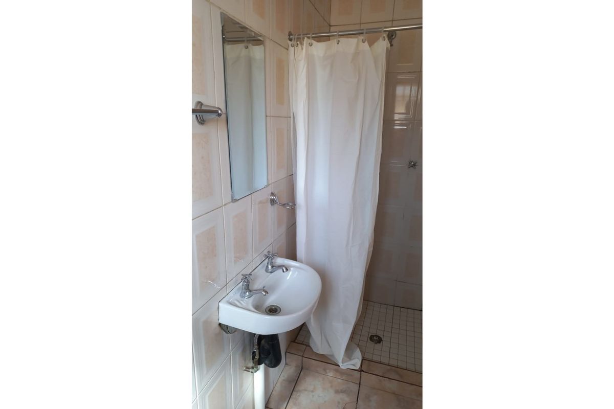 A compact bathroom featuring a wall-mounted basin, a shower area with a curtain, and dated ceramic wall and floor tiles.