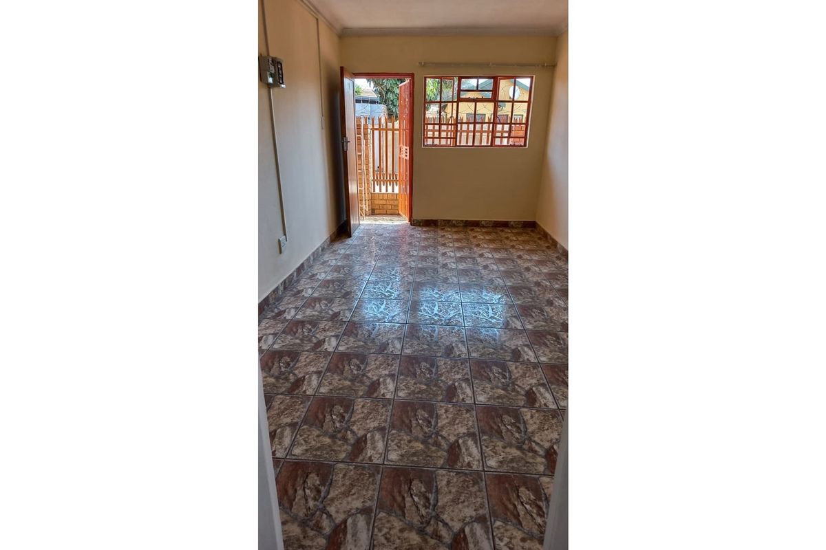 An empty bedroom featuring tiled flooring, a window with metal frames, and direct access to an outdoor area.