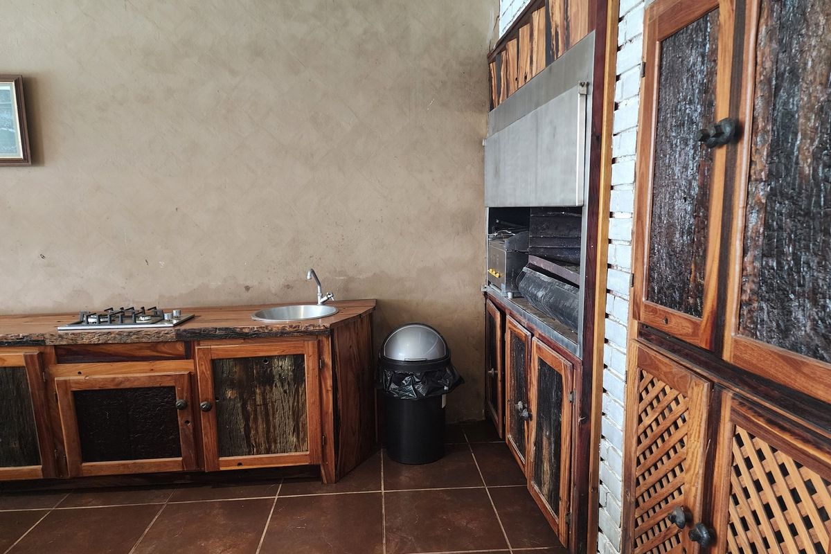 Rustic outdoor kitchen area featuring custom timber cabinetry, a built-in braai or grill, integrated gas hob, and a stainless steel prep sink.