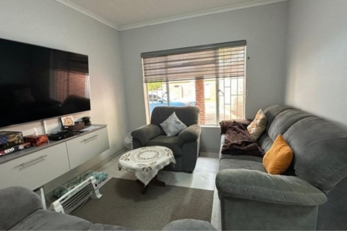 A comfortable living room featuring tiled flooring, a wall-mounted media console, and a large window with fitted blinds providing natural light.