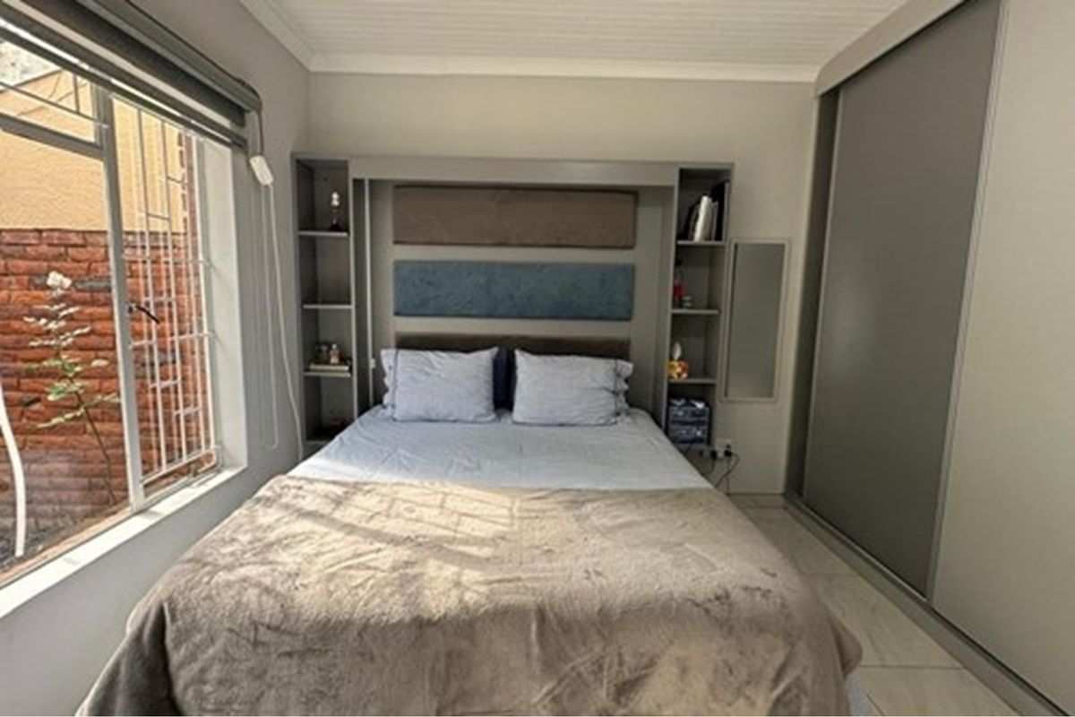 A well-maintained bedroom featuring built-in cabinetry, integrated shelving, and sliding door wardrobes, offering efficient storage and a clean, functional layout.