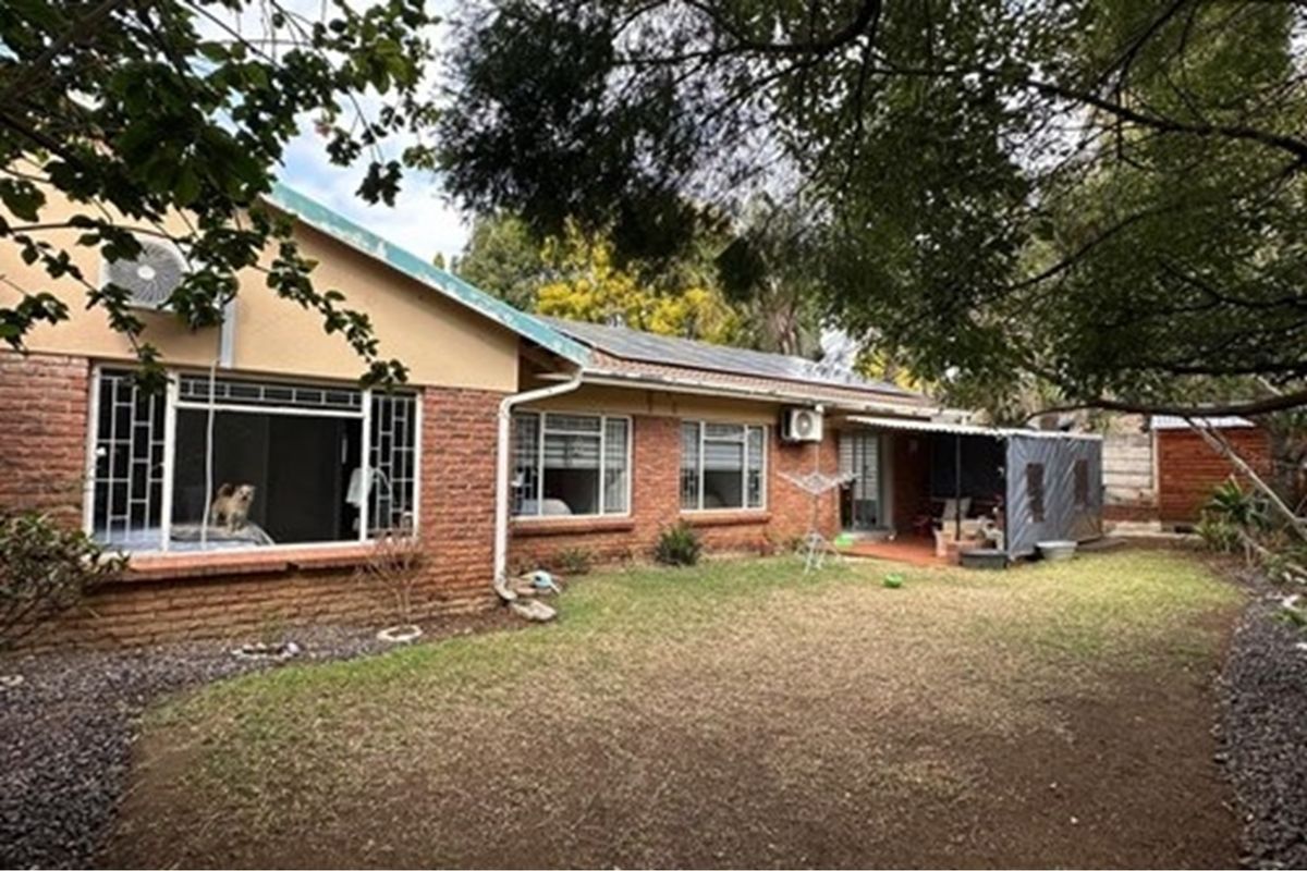 Rear view of the townhouse featuring a brick facade, covered patio area, and a private garden space with established trees.