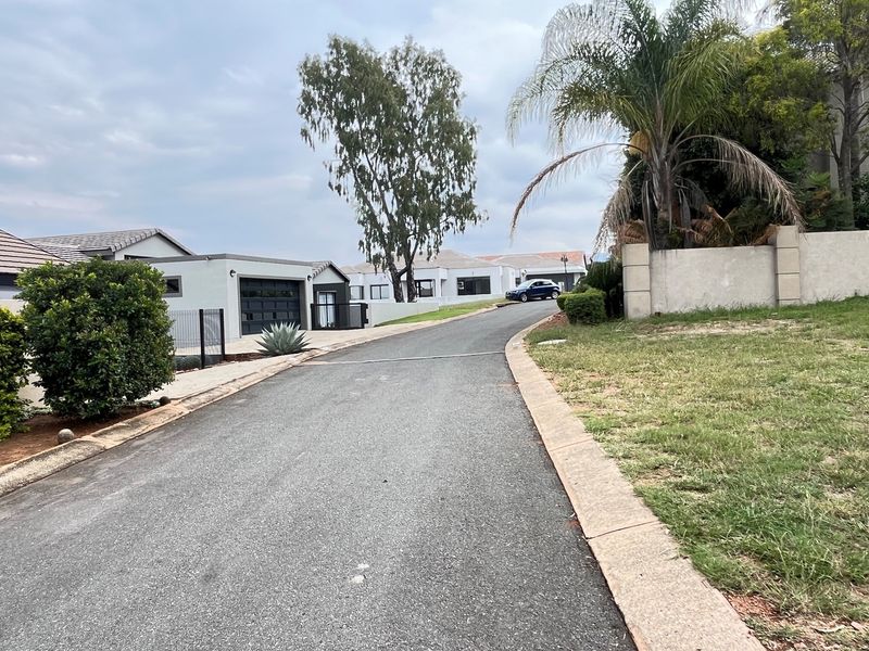A view of the residential street approach featuring paved roads, concrete curbing, and established boundary walls within the estate.