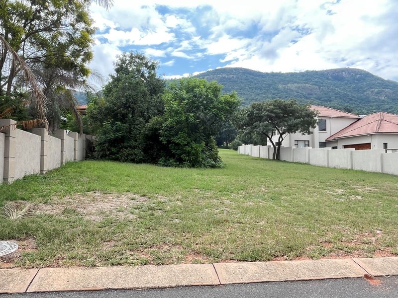 A vacant residential plot featuring established perimeter walls, mature trees, and mountain views, ready for development.