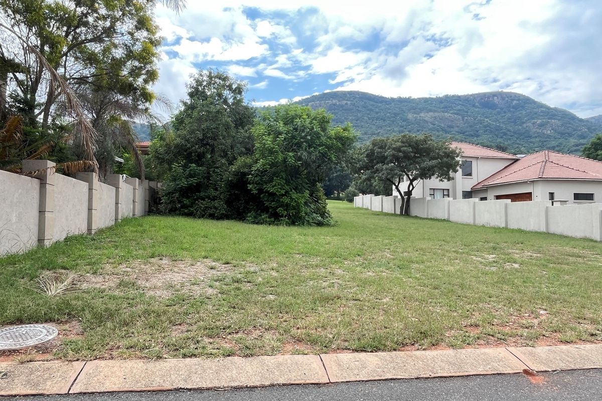 A vacant residential plot featuring established perimeter walls, mature trees, and mountain views, ready for development.