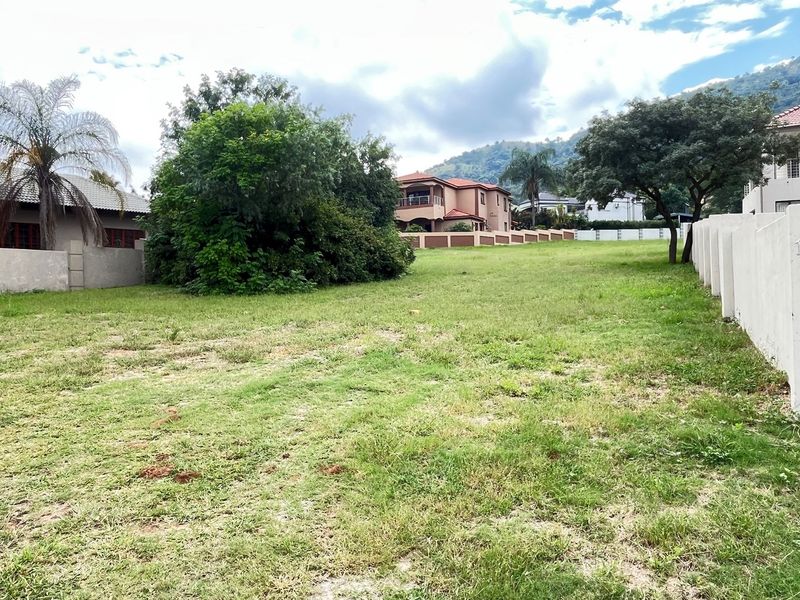 A vacant residential plot featuring established boundary walls, mature trees, and a grass lawn in a developed neighborhood setting.
