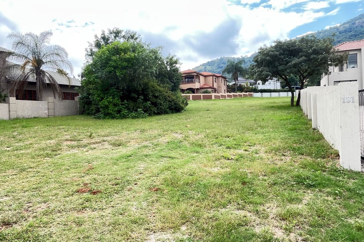 A vacant residential plot featuring established boundary walls, mature trees, and a grass lawn in a developed neighborhood setting.