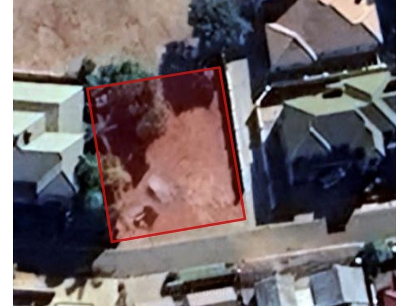 An aerial view of a vacant residential land plot highlighted in red, situated within an established neighborhood.