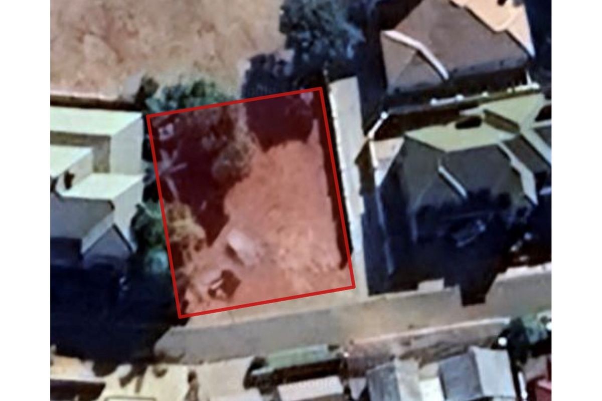 An aerial view of a vacant residential land plot highlighted in red, situated within an established neighborhood.