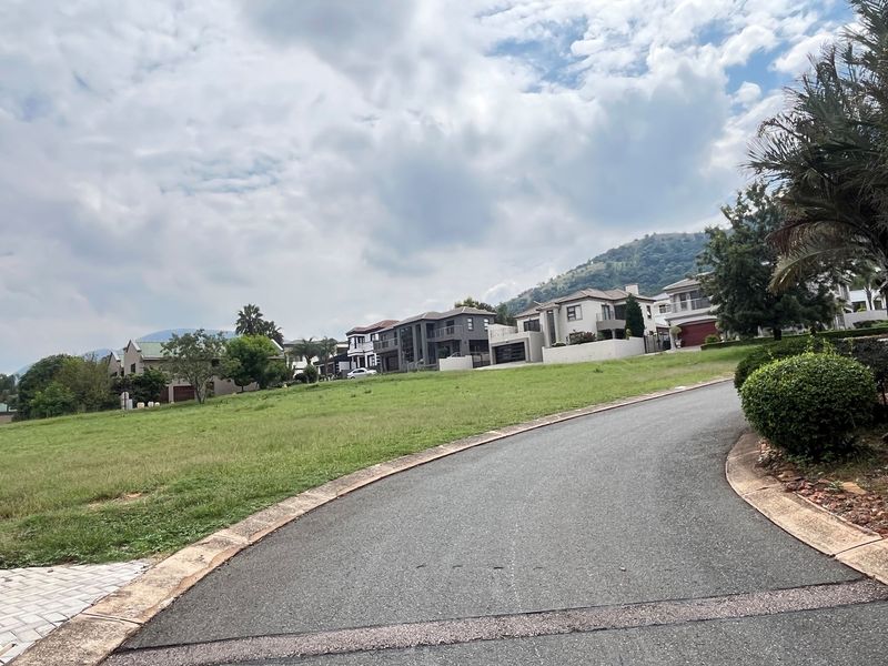 A view of the street and surrounding residential neighborhood, showcasing the paved road and sloped grass verge of the vacant land.