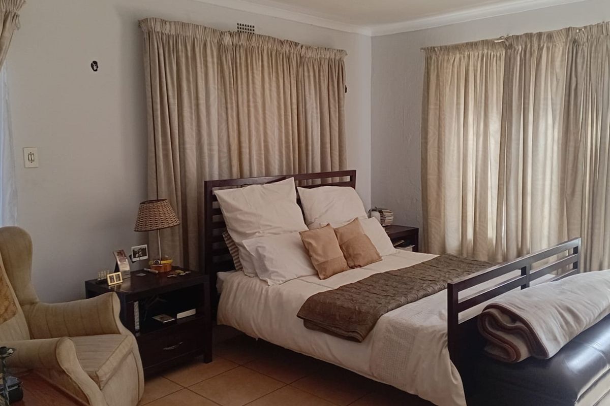 A bedroom featuring tiled flooring, neutral wall tones, and floor-to-ceiling curtains, providing a functional and comfortable sleeping space.