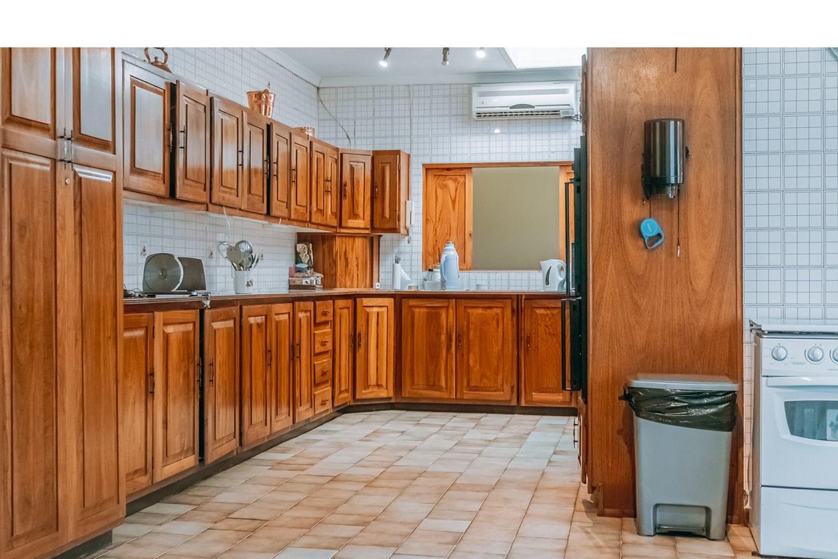 A functional kitchen featuring extensive wooden cabinetry, tiled backsplash, and tiled flooring, equipped with a wall-mounted air conditioning unit.