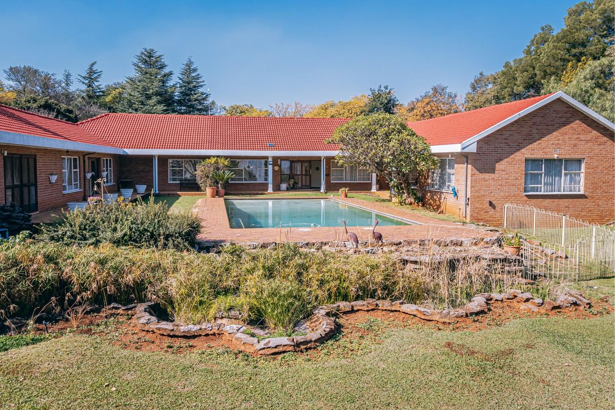 A spacious U-shaped farmhouse featuring a central swimming pool, brick exterior, red tiled roof, and established garden surroundings.