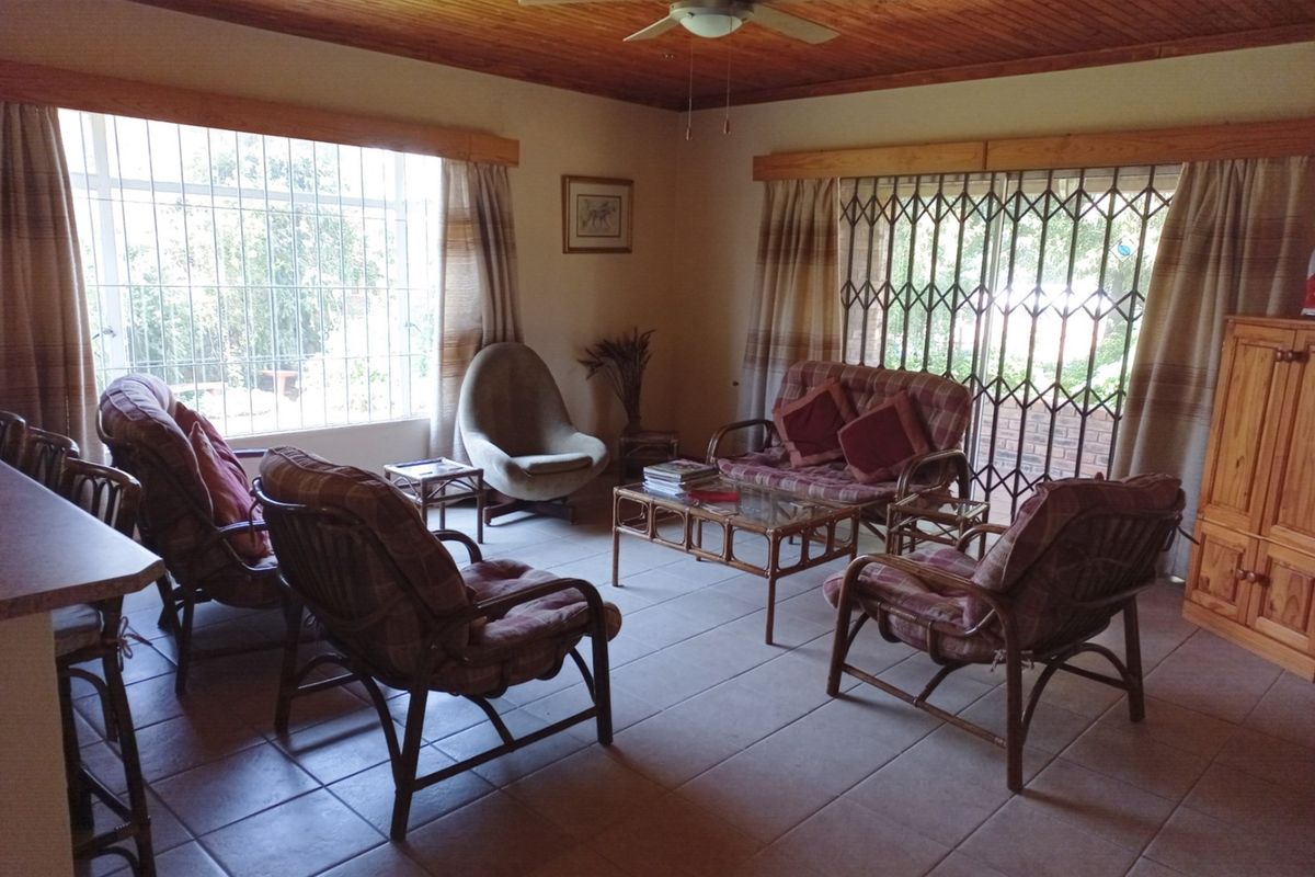 A spacious living room featuring tiled flooring, a timber-paneled ceiling, and large windows with security bars, providing ample natural light.