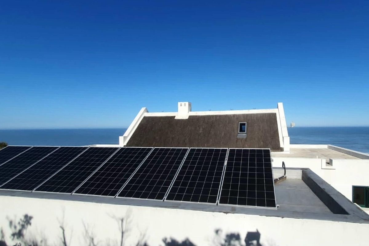 An elevated view of the property roof featuring a modern solar panel array and a traditional thatched roof section overlooking the ocean.