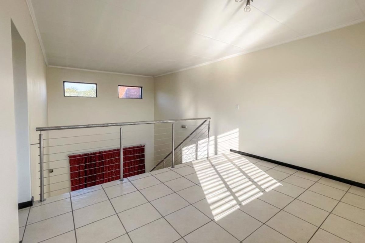 An open-plan mezzanine living area featuring tiled flooring, a modern stainless steel balustrade, and high-level clerestory windows providing natural light.