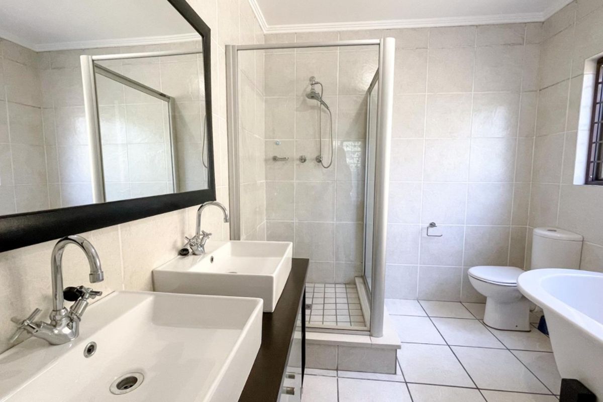 Modern bathroom featuring a double vanity, glass-enclosed shower, and a freestanding bathtub with neutral wall and floor tiling.