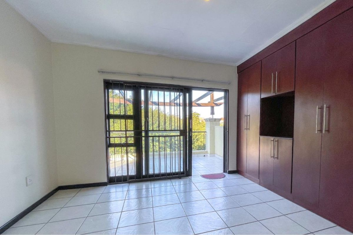 Spacious bedroom featuring built-in cupboards, tiled flooring, and a sliding door providing access to a private balcony.