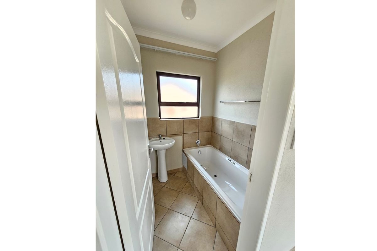 A functional bathroom featuring a built-in bathtub with tiled surround, a pedestal basin, and ceramic floor tiling.