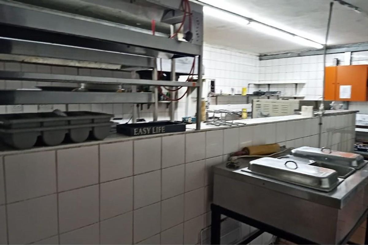 A functional commercial-style kitchen featuring tiled walls, stainless steel shelving, and industrial food preparation equipment, suitable for high-volume catering or restaurant use.