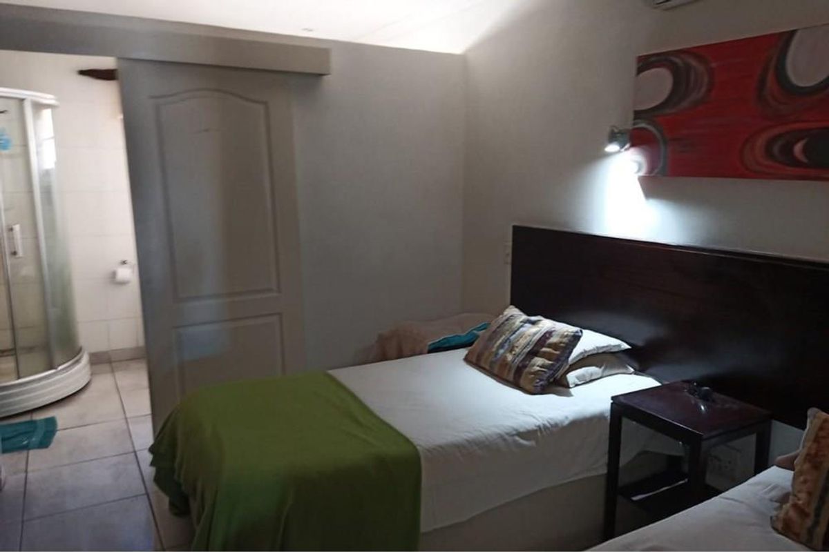 A functional bedroom featuring tiled flooring, a sliding door leading to an en-suite shower, and wall-mounted lighting fixtures.
