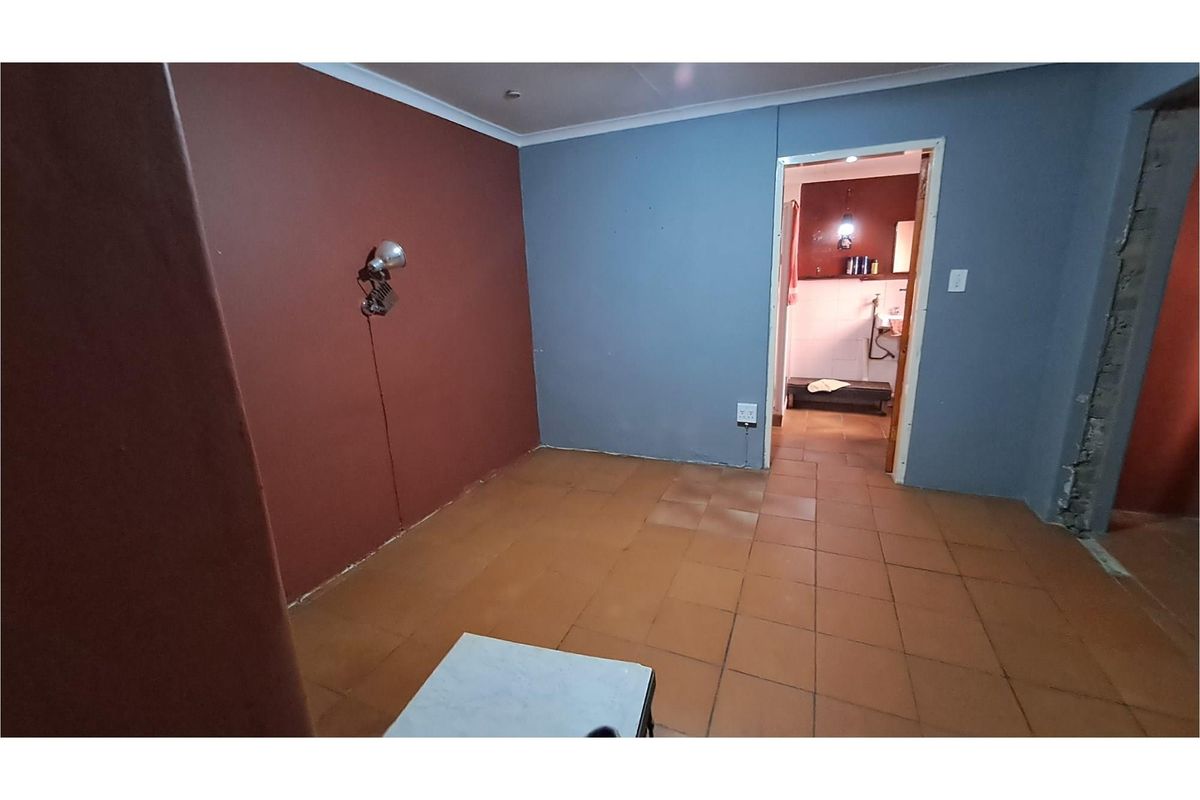 An interior view of a room featuring terracotta floor tiles and painted walls, with a doorway leading to an adjacent bathroom area.