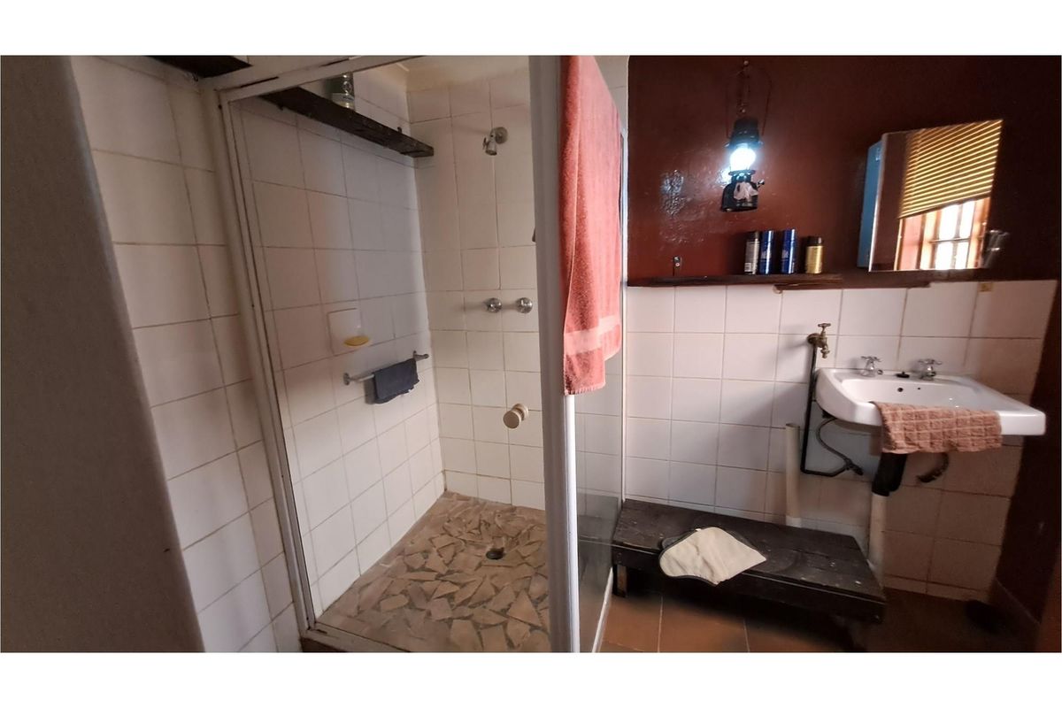 A dated bathroom featuring a glass-enclosed shower, wall-mounted basin with exposed plumbing, and tiled wall finishes.