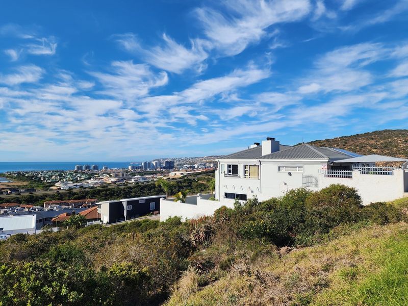 Elevated view of a residential property featuring a modern home with a tiled roof, overlooking the coastal landscape and surrounding neighborhood.