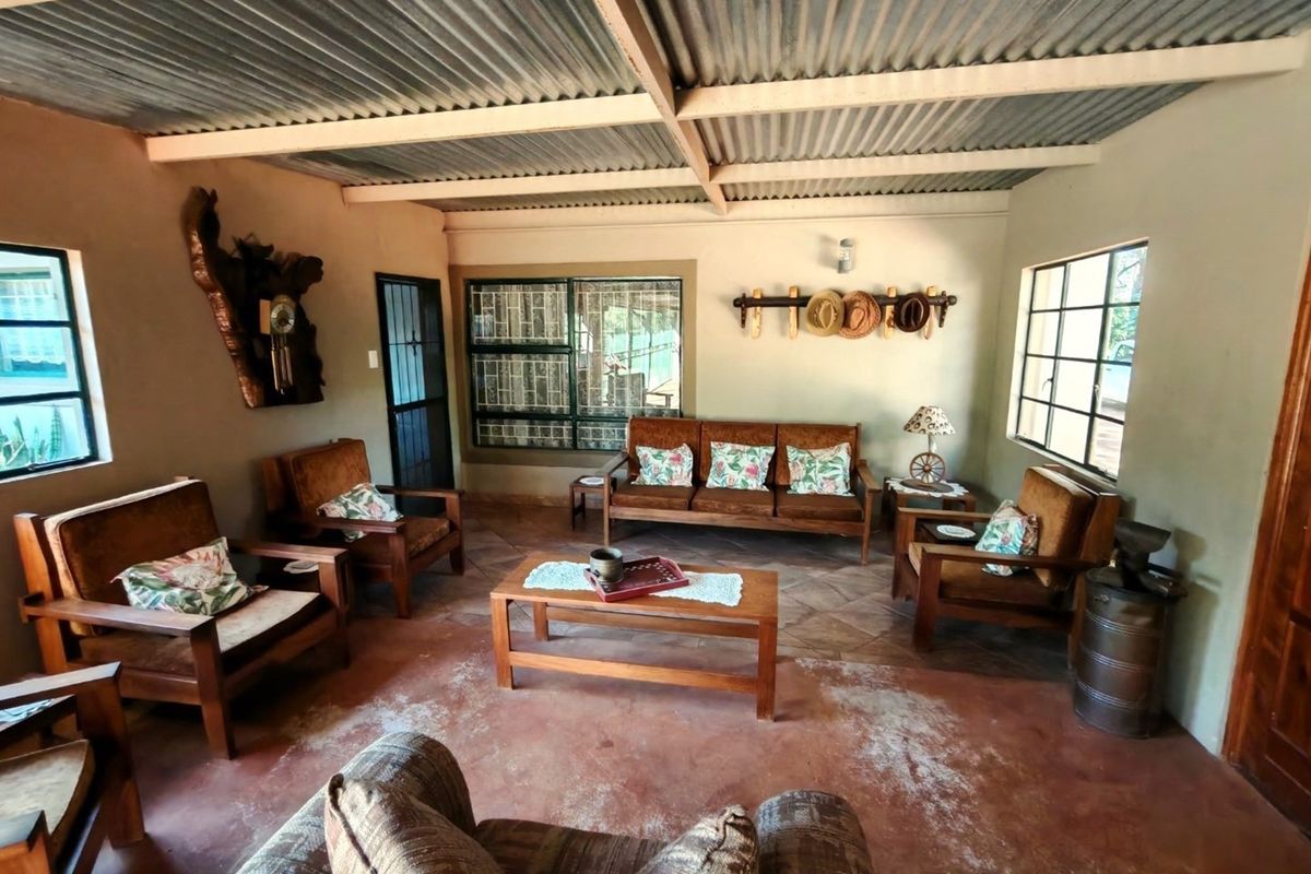 A rustic living area featuring exposed corrugated metal roofing, tiled flooring, and large windows providing natural light.