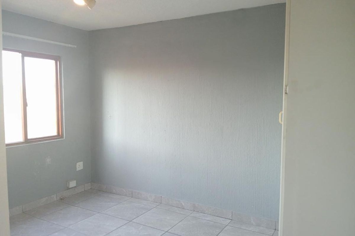 A vacant bedroom featuring grey painted walls, tiled flooring, and a window with a wooden frame.