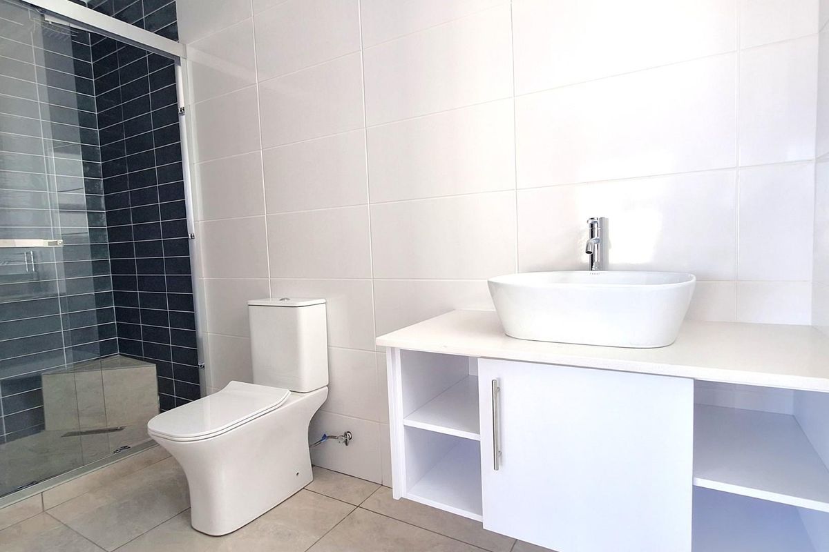 Modern bathroom featuring a white vanity with a vessel sink, a close-coupled toilet, and a glass-enclosed shower with dark accent tiling.