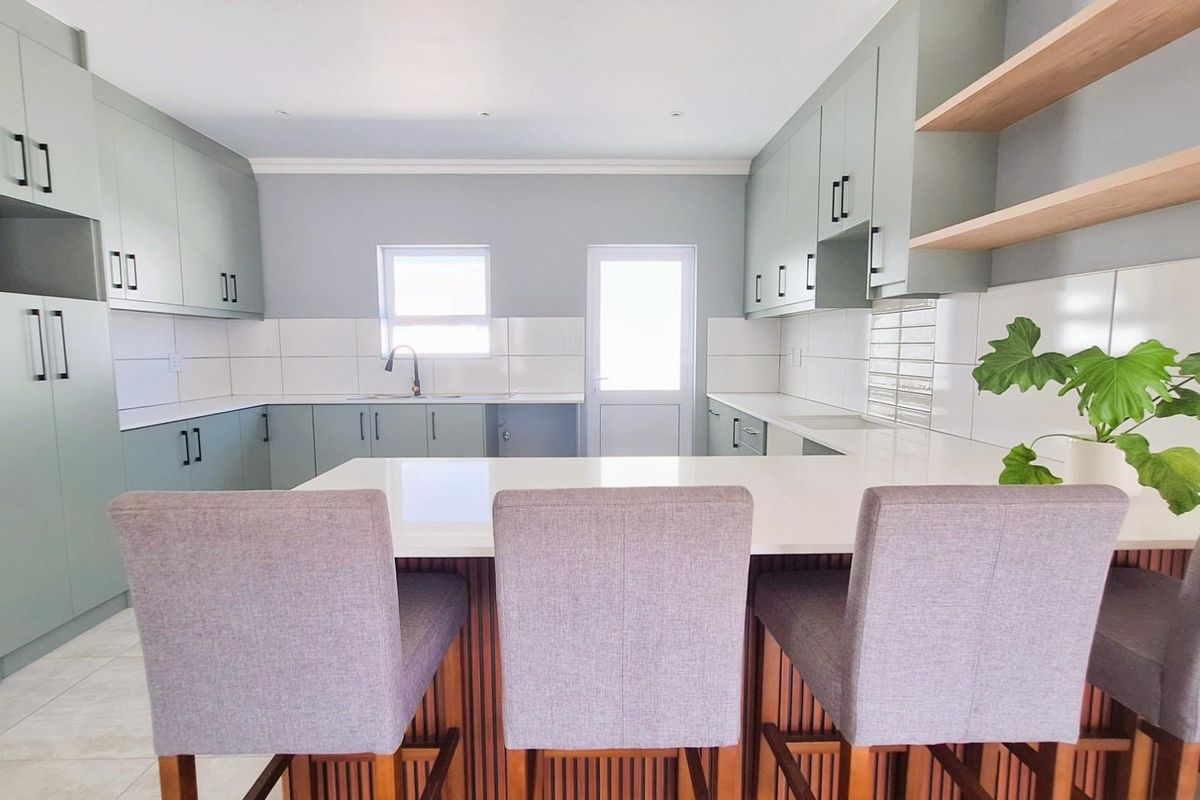 Modern kitchen featuring sage green cabinetry, white stone countertops, a breakfast bar, and open shelving.