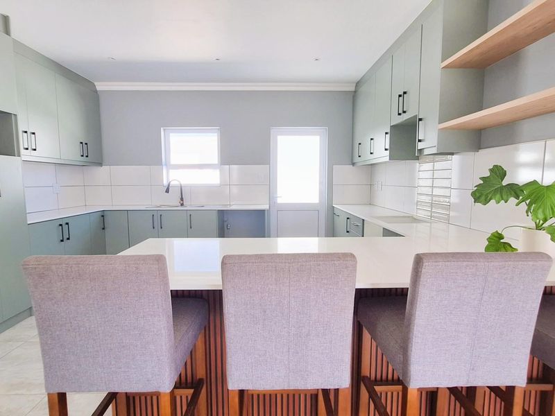 Modern kitchen featuring sage green cabinetry, white stone countertops, a breakfast bar, and open shelving.