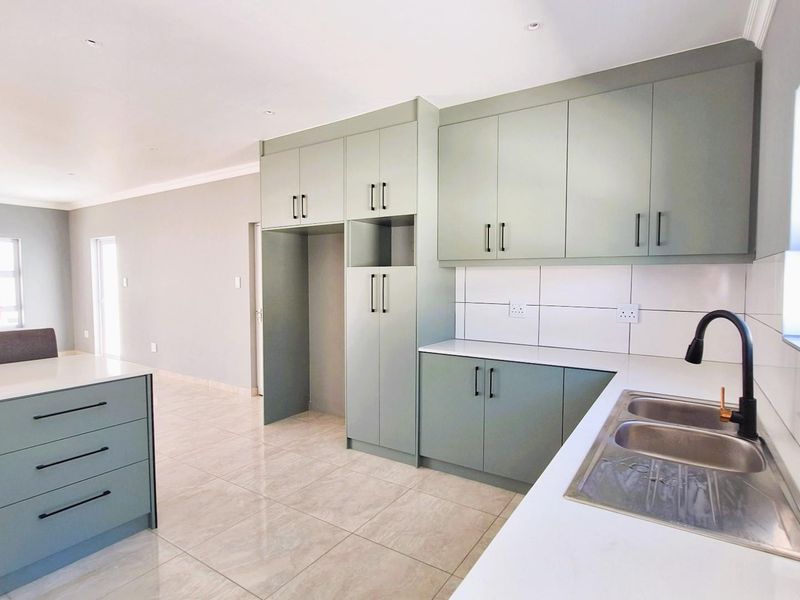 Modern open-plan kitchen featuring sage green cabinetry, white countertops, a double sink with a matte black faucet, and tiled flooring.