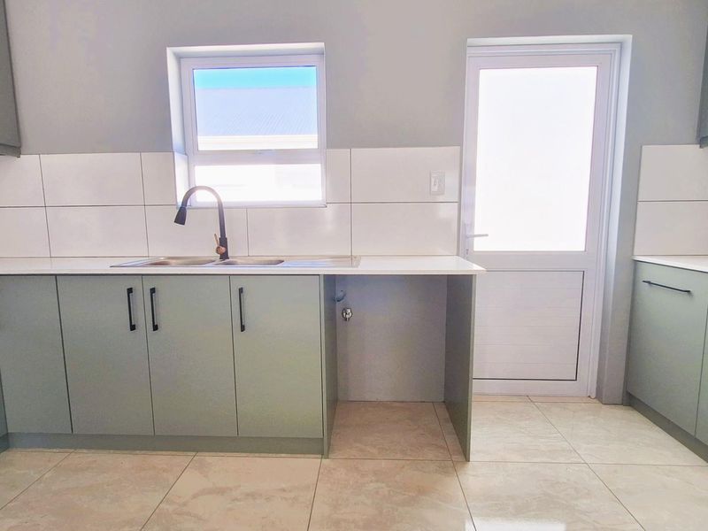 Modern kitchen featuring light green cabinetry, white countertops, tiled backsplash, double sink with matte black faucet, and direct access to the exterior.