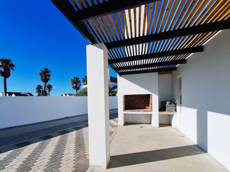 A covered outdoor patio area featuring a built-in brick braai or fireplace, concrete flooring, and a modern slatted timber pergola structure.