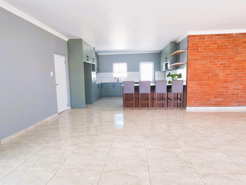 Spacious open-plan kitchen and living area featuring modern cabinetry, a breakfast bar, and a striking exposed brick feature wall.