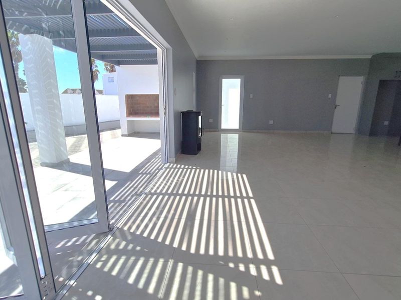 Spacious open-plan living area featuring large sliding doors that open onto a covered patio with a built-in braai.