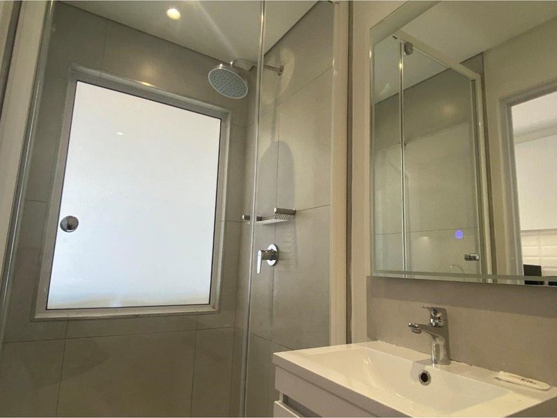 Modern bathroom featuring a glass-enclosed shower, wall-mounted vanity with basin, and a large mirror.