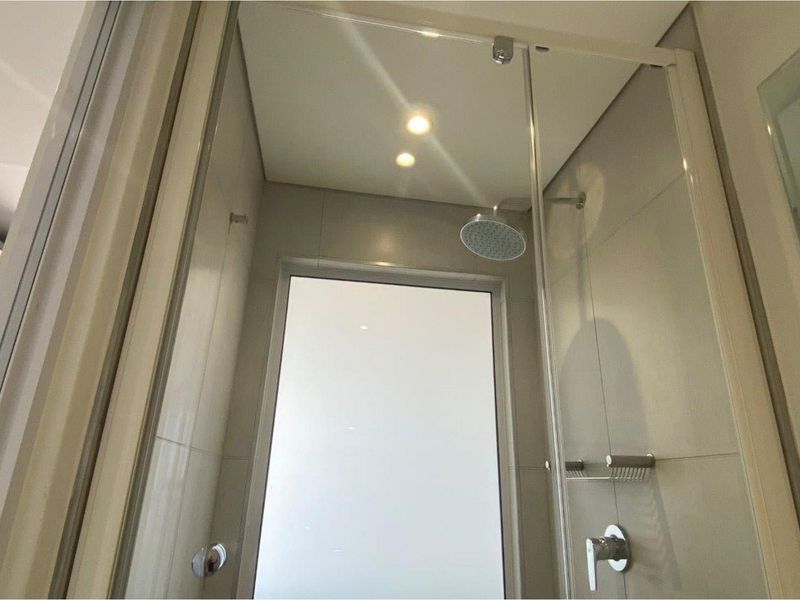 Modern shower enclosure featuring a rainfall showerhead, glass door, and neutral wall tiling.
