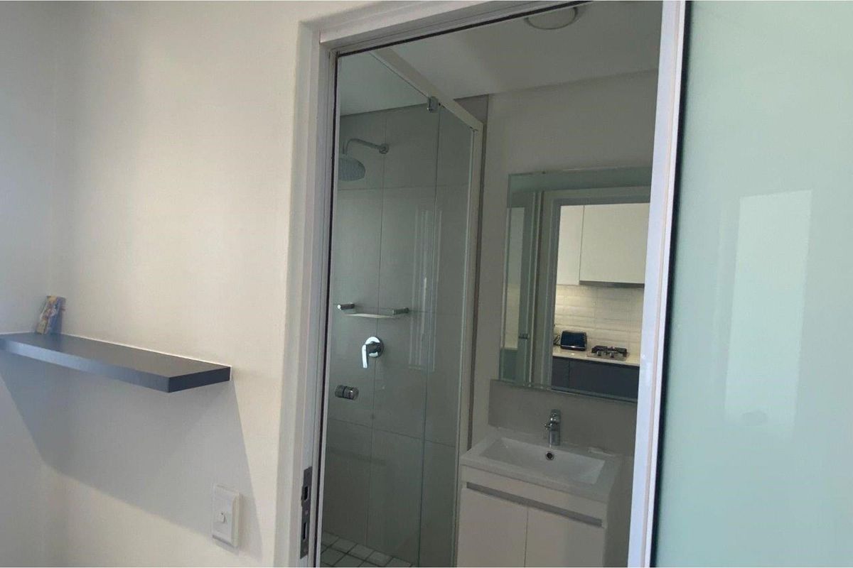 A modern bathroom featuring a glass-enclosed shower, a vanity with a basin, and a wall-mounted mirror, viewed from an adjacent room.