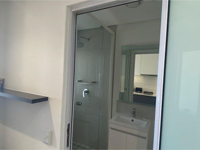 A modern bathroom featuring a glass-enclosed shower, a vanity with a basin, and a wall-mounted mirror, viewed from an adjacent room.