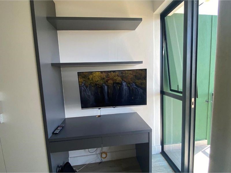 A compact home office nook featuring a built-in desk with integrated shelving and direct access to an outdoor balcony through a glass door.