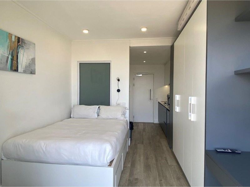 A compact studio bedroom featuring built-in cabinetry, recessed lighting, and a modern kitchenette area with sleek finishes.