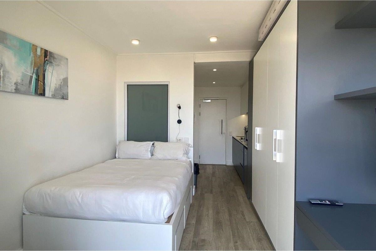 A compact studio bedroom featuring built-in cabinetry, recessed lighting, and a modern kitchenette area with sleek finishes.