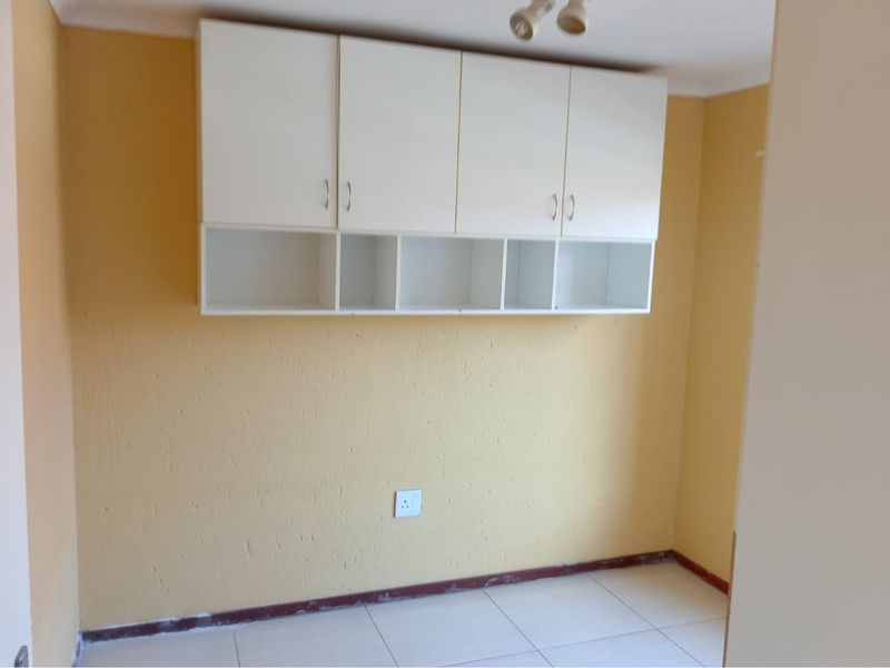 A compact bedroom featuring wall-mounted storage cabinetry, tiled flooring, and a neutral yellow wall finish, ready for personalization.