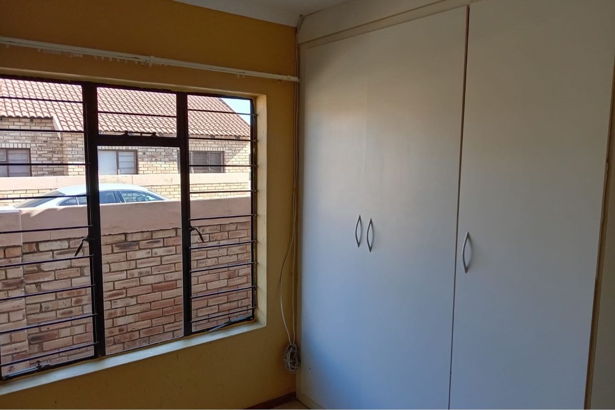 A bedroom featuring a built-in wardrobe and a window with security bars, requiring cosmetic updates to the wall finishes.