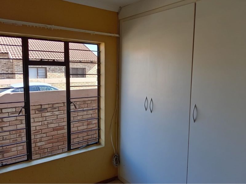 A bedroom featuring a built-in wardrobe and a window with security bars, requiring cosmetic updates to the wall finishes.