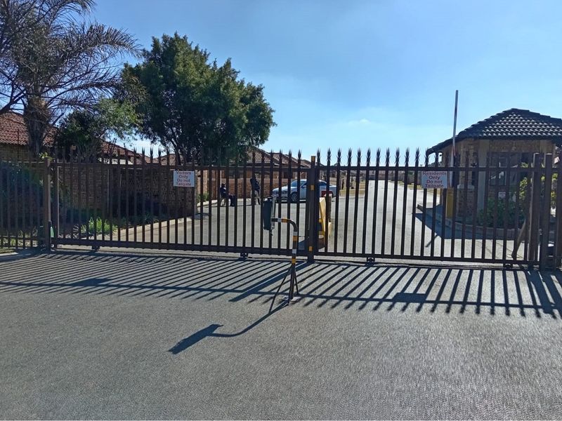Secure gated entrance to the townhouse complex featuring automated security gates, access control infrastructure, and a guard house.